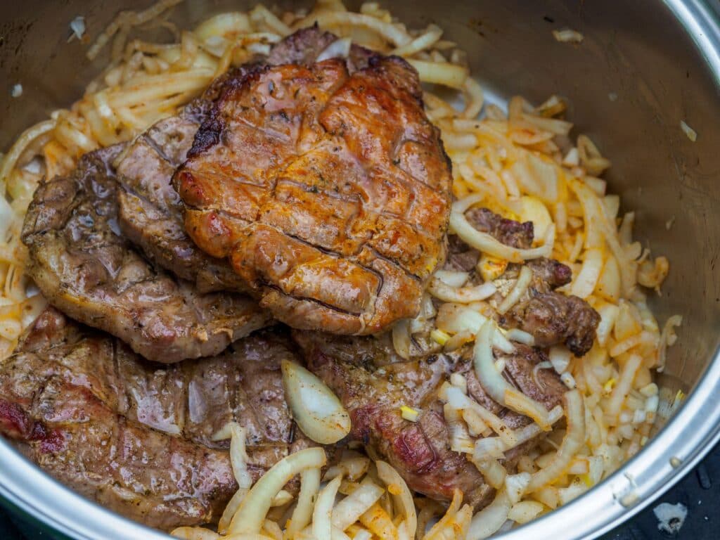 Bifes cozidos servidos com cebolas fatiadas em uma panela