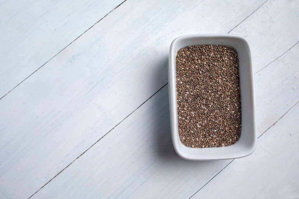 Sementes de chia em uma tigela branca sobre uma superfície de madeira clara