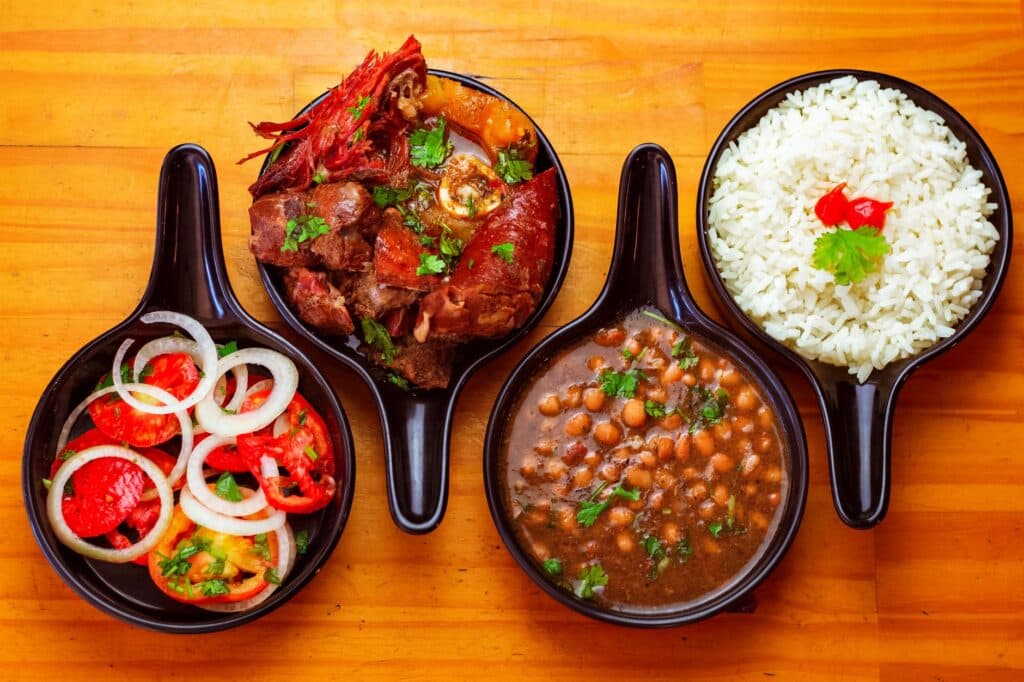 Pratos brasileiros com arroz, feijão, carne e salada servidos em tigelas pretas