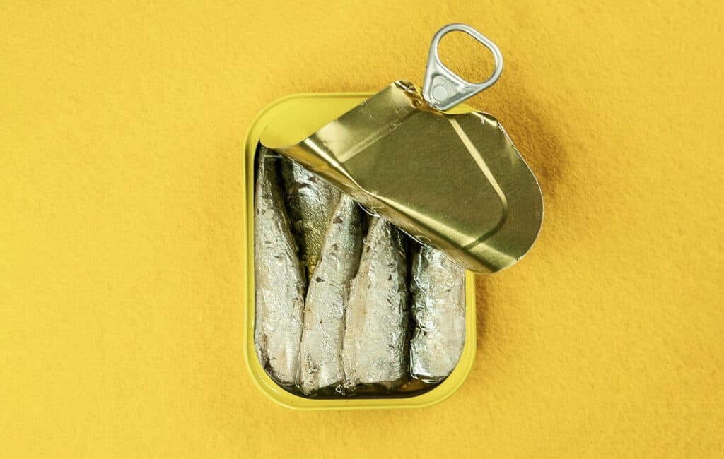 Lata de sardinha aberta, com os peixes à mostra, sobre fundo amarelo