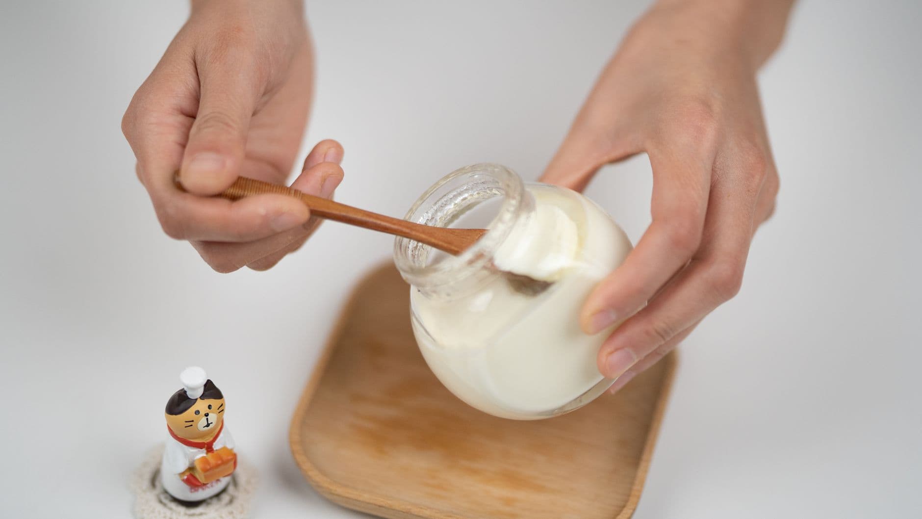 Pessoa comendo iogurte natural branco de um pote de vidro com colher de bambu