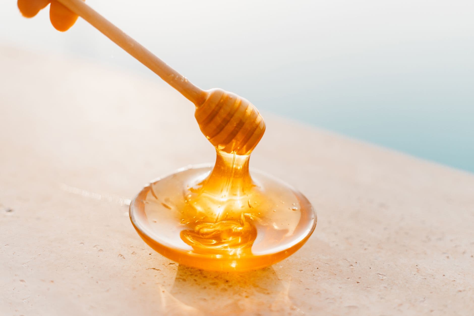 Mel dourado escorrendo de uma colher de madeira sobre um prato de vidro