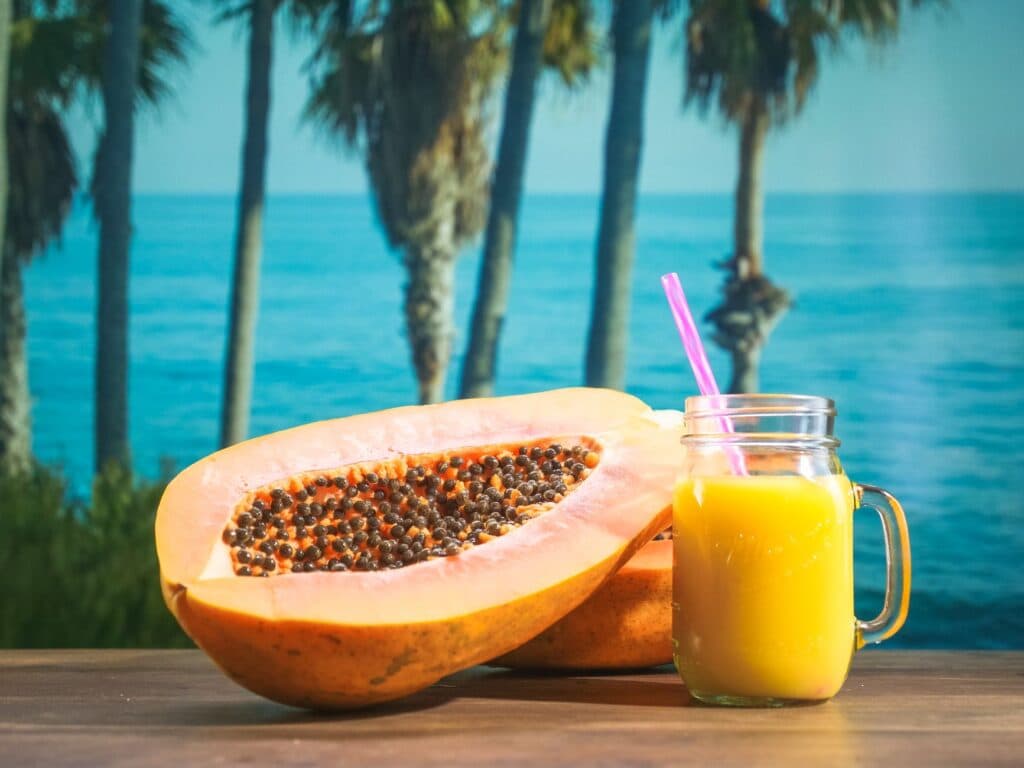 Mamão fresco ao lado de um copo de suco de frutas tropicais